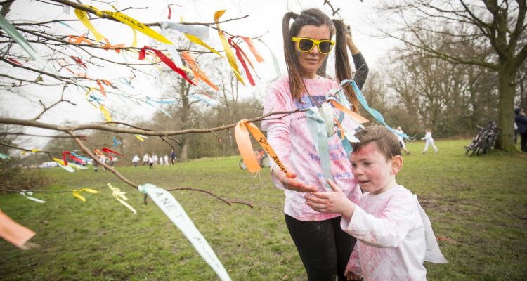 Young woman and boy hanging ribbon on tree of dedication at ObstaColour Run