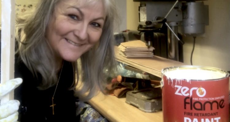 Artist Lindi holding a painted wooden frame around her head, smiling and looking at the camera
