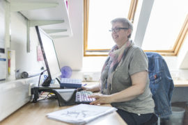 A woman smiling sat at a desk and looking at her computer