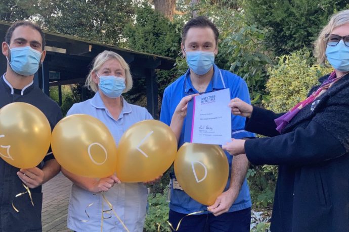 Three staff members and the IIP assessor holding gold balloons which spell GOLD.