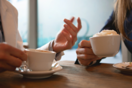 Two people's hands holding cups of coffee next to each other at a table