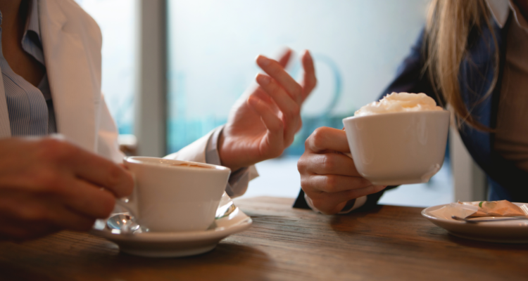 Two people's hands holding cups of coffee next to each other at a table